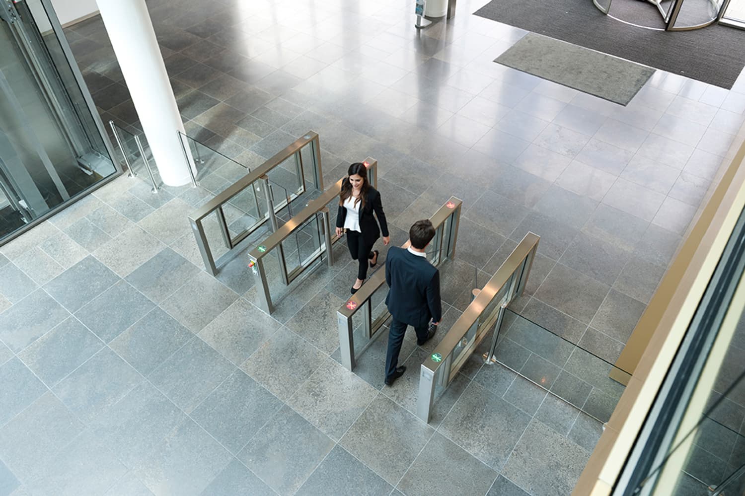 Two people using a turnstile in a modern building lobby.